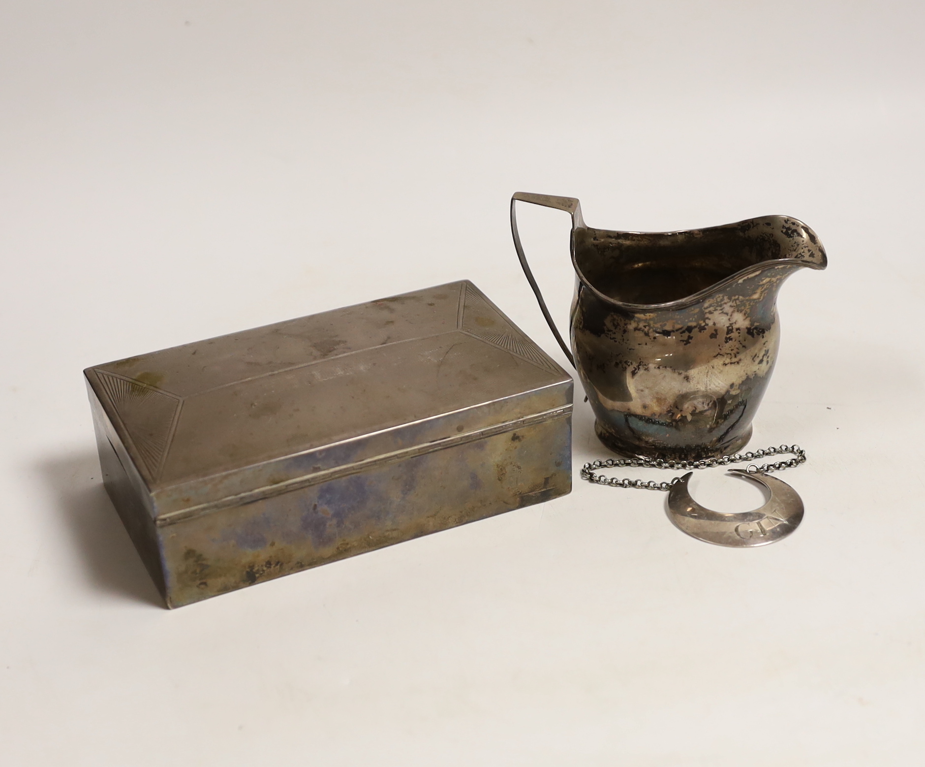 A George V Art Deco silver mounted rectangular cigarette box, with engraved inscription, Birmingham, 1932, 15.1cm, a Georgian silver cream jug, maker possibly William Welch II of Exeter? and a Georgian silver crescent 'G